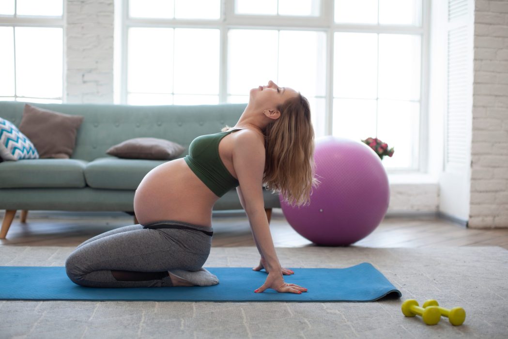 Portrait of young pregnant woman working out indoors. Focus on belly